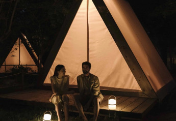 Two people sitting outside a lit safari cabin tent at night at Wecamp Santa Cristina in Spain.