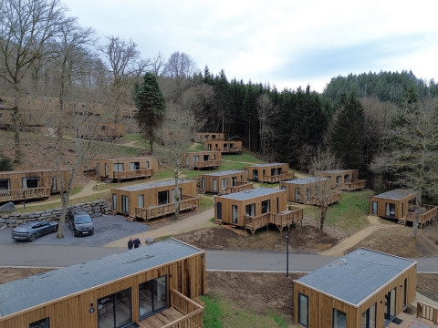 Luchtfoto van houten huisjes op vakantiepark Hameau de la Semois, omgeven door bos in Luxemburg, België.