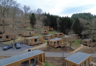 Luftbild von Holzhütten im Ferienpark Hameau de la Semois, umgeben von Wald in Luxemburg, Belgien.