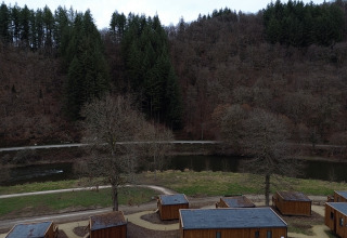 Blick auf das Ferienpark Hameau de la Semois mit Holzhütten, Fluss und bewaldeten Hügeln in Belgien.
