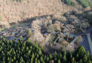 Luchtfoto van vakantiepark Hameau de la Semois in België met houten huisjes tussen de bomen.