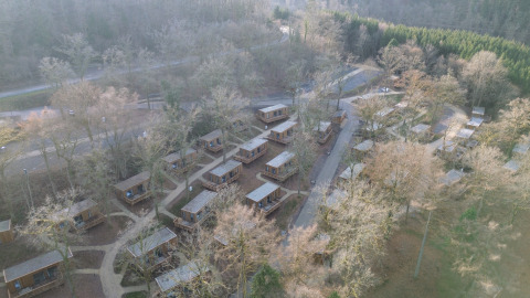 Luchtfoto van vakantiepark Hameau de la Semois in België met huisjes tussen bomen en wandelpaden.