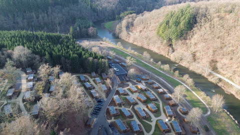 Luftaufnahme des Ferienparks Hameau de la Semois in Belgien, umgeben von Wald, Hütten und einem Fluss.