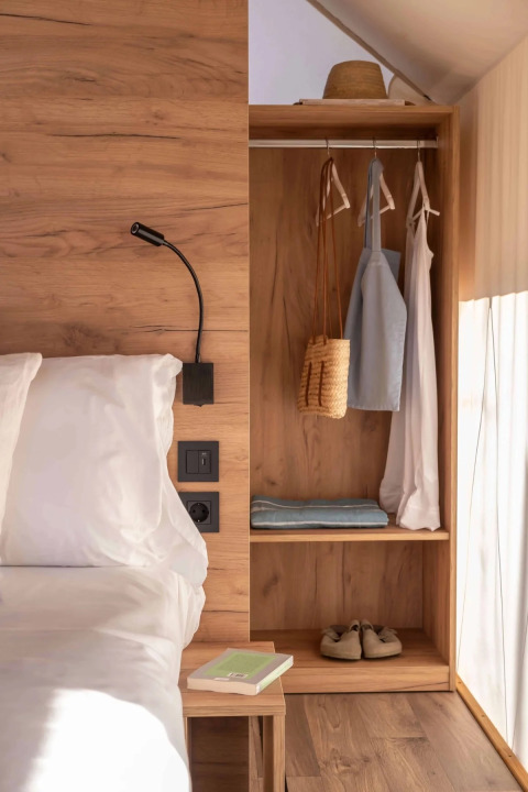 Luxe safaritent interieur met houten meubels, open kast, hangende kledij en natuurlijk licht.