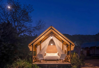 Verlicht safaritent met een tweepersoonsbed en stoelen 's avonds bij Wecamp Santa Cristina in Spanje.