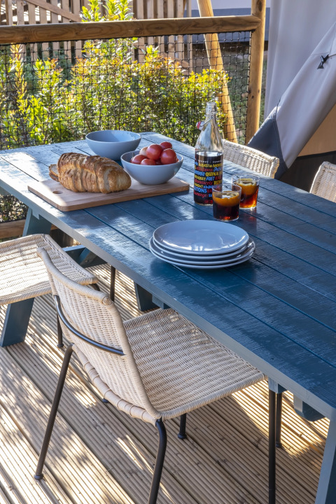 Buitentafel met borden, brood, tomaten en drankjes op het terras van een safaritent.