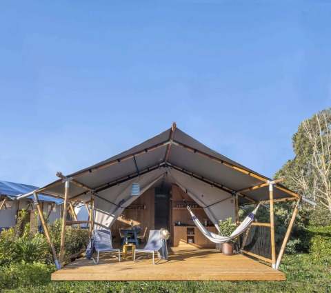 Safari tent met houten terras, hangmat, loungestoelen en zitgedeelte in een groene omgeving.