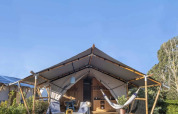 Safari tent with wooden deck, hammock, lounge chairs and outdoor seating set in natural surroundings.