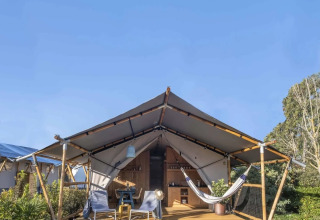 Safari tent met houten terras, hangmat, loungestoelen en zitgedeelte in een groene omgeving.