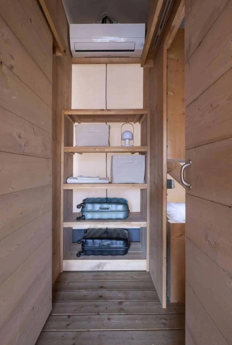 Interieur van Lodge 'Family Duplex' bij Wecamp Santa Cristina, Spanje, met houten planken en koffers.