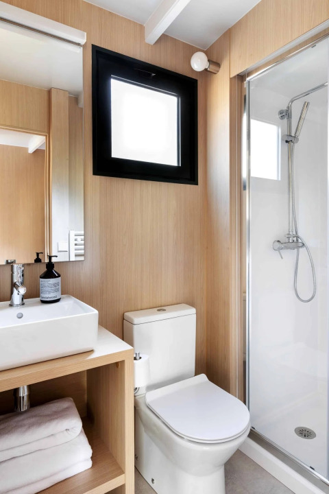 Moderne badkamer in een lodge met houten panelen, douche, toilet en wastafel met handdoeken.