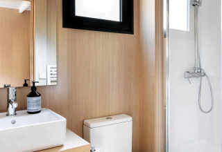 Moderne badkamer in een lodge met houten panelen, douche, toilet en wastafel met handdoeken.
