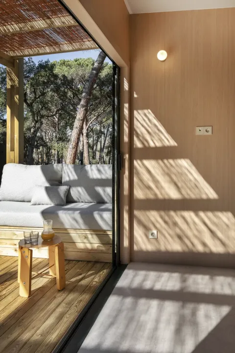 Zonlicht valt binnen in een moderne houten lodge bij Wecamp Santa Cristina, Spanje, met een comfortabele sofa.