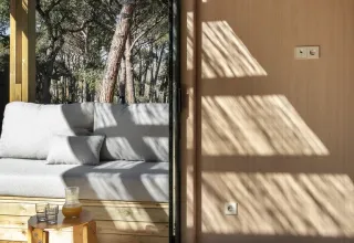 Zonlicht valt binnen in een moderne houten lodge bij Wecamp Santa Cristina, Spanje, met een comfortabele sofa.