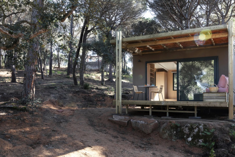 Mobil-home Couple Plus dans une forêt, avec terrasse couverte, table et chaises, en plein jour.