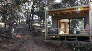 Mobil-home Couple Plus dans une forêt, avec terrasse couverte, table et chaises, en plein jour.