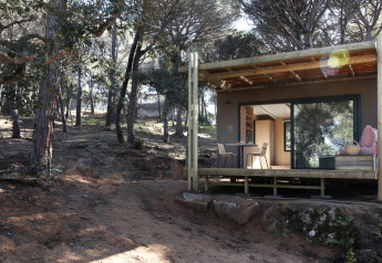 Mobil-home Couple Plus dans une forêt, avec terrasse couverte, table et chaises, en plein jour.