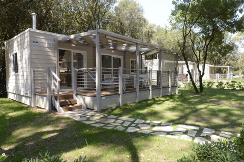 Modern mobiel huis met ruime, overdekte veranda, omgeven door bomen en zonovergoten grasveld.