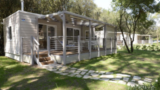 Modern mobiel huis met ruime, overdekte veranda, omgeven door bomen en zonovergoten grasveld.