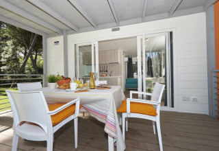 Glamping-terras met gedekte ontbijttafel, vier stoelen met oranje kussens en zicht op moderne keuken.