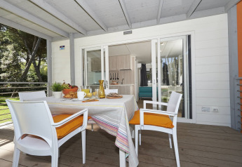 Terrasse de glamping avec table dressée pour le petit-déjeuner, quatre chaises et vue sur cuisine moderne.