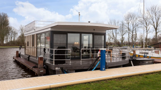 Péniche Houseboat Elysium avec terrasse sur le toit, amarrée au quai dans un cadre paisible et verdoyant.