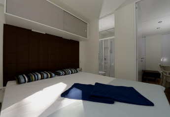 Mobile home bedroom with double bed, striped pillows, brown headboard and bathroom visible through door.