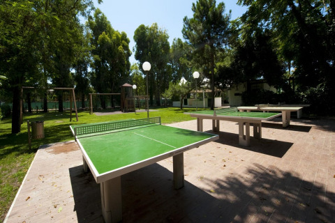 Buiten tafeltennistafels in een groen park bij een glampingaccommodatie, omgeven door bomen.