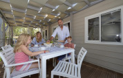 Family enjoying a meal together on the deck of a mobile home under a partially covered roof.