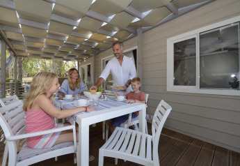 Family enjoying a meal together on the deck of a mobile home under a partially covered roof.