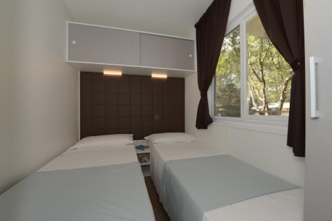 Slaapkamer in een stacaravan met twee eenpersoonsbedden, groot raam met gordijnen en modern interieur.