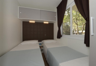 Slaapkamer in een stacaravan met twee eenpersoonsbedden, groot raam met gordijnen en modern interieur.
