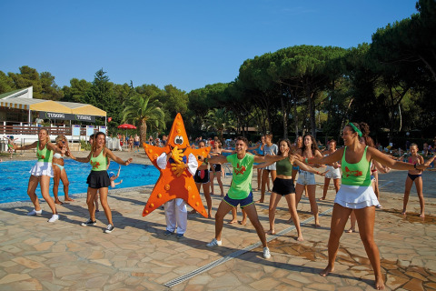 Groep mensen danst vrolijk bij het zwembad van een glamping-accommodatie met een zeester mascotte.
