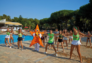 Menschen tanzen fröhlich mit einem Seestern-Maskottchen am Pool eines Glamping-Resorts.