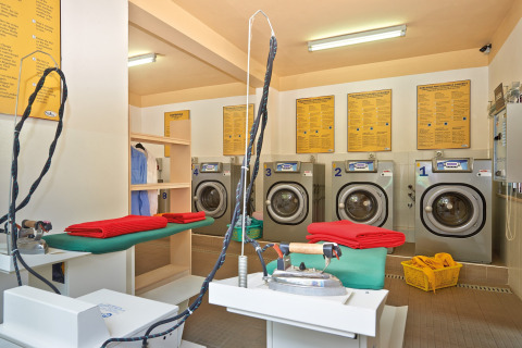 Wasserette bij een glamping-accommodatie met moderne wasmachines, strijktafels en rode handdoeken.