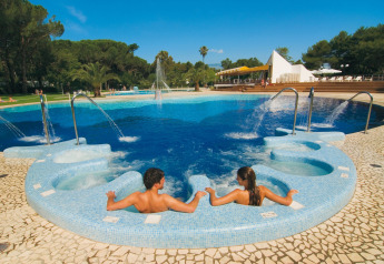 Two people relax in a jacuzzi by the outdoor pool at Baia Domizia Villaggio Camping C3 in Italy.