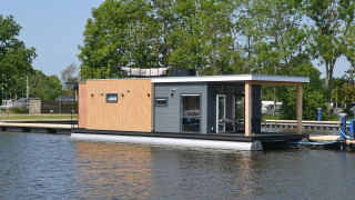 Moderne woonboot aan het water met bomen op de achtergrond, RiggelBrug Sneekermeer op een zonnige dag.