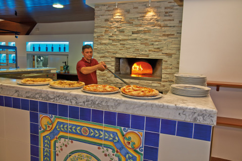 Een pizzabakker haalt een versgebakken pizza uit een houtoven in de keuken van een mobiel huis.