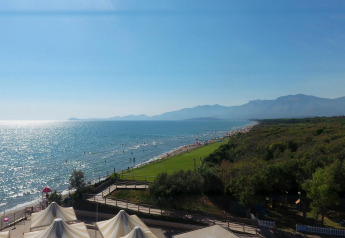 Glamping site by the sea with tents, grassy area, and a scenic coastal view with mountains beyond.