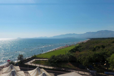 Uitzicht op het strand vanaf een glampinglocatie met tenten, groene velden, zee en bergen op de achtergrond.