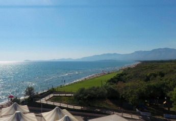 Vue sur la plage depuis un site de glamping avec tentes, espaces verts, mer et montagnes en arrière-plan.