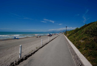 Brede strandpromenade bij een stacaravanpark met zandstrand, zee en een heldere blauwe lucht.