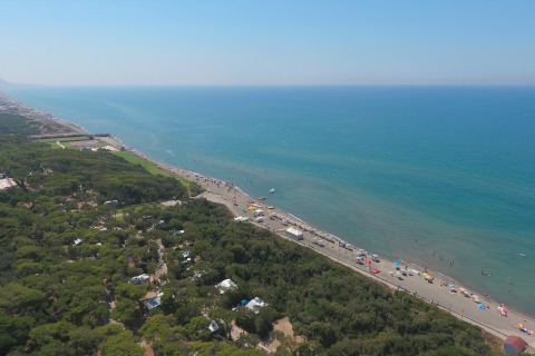 Luftaufnahme eines Mobilheimplatzes am Strand mit grüner Vegetation und blauem Meer im Hintergrund.