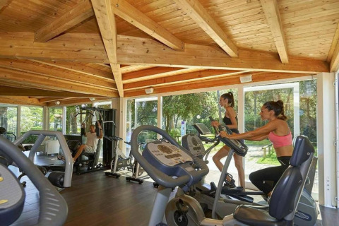 Mensen sporten in een fitnessruimte met houten plafond en grote ramen in een stacaravan omgeving.
