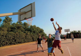 Des adolescents jouent au basket sur un terrain extérieur entouré d’arbres lors d’un séjour en glamping.