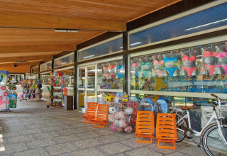 Uitzicht op een glampingwinkel met badkleding, strandartikelen, ballen en fietsen buiten de etalage.