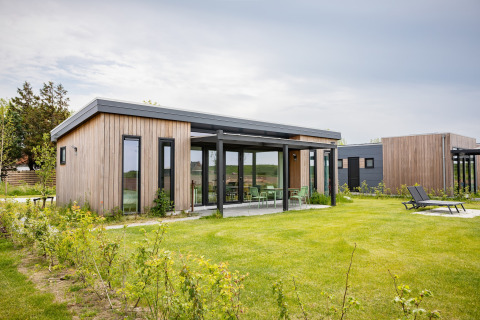 Park Wijdenes 4-lodge med moderne træfacade, store vinduer og grøn have under en overskyet himmel.