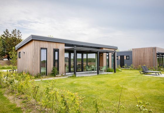Park Wijdenes 4-lodge med moderne træfacade, store vinduer og grøn have under en overskyet himmel.