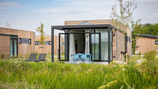Moderne lodge Park Wijdenes 2 med træfacade, udendørs siddeområde og grøn natur omkring bygningen.