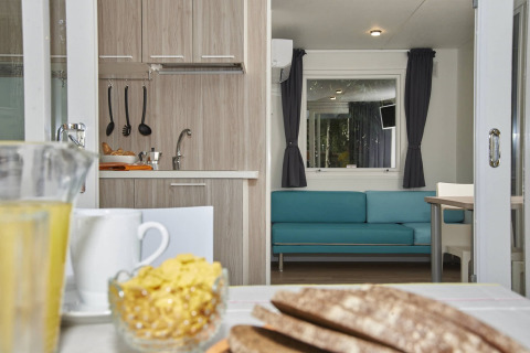 Binnenkant van glamping accommodatie met eettafel, keuken en een turquoise bank bij het raam.